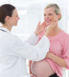 Female doctor examining thyroid glands of pregnant woman in hospital