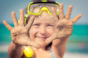 Happy child playing on the beach. Kid showing sand on hands. Summer vacations concept