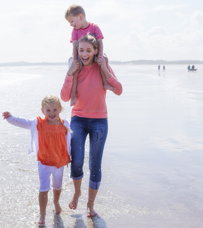 Young single mother at the beach with her son and daughter. They are laughing and are barefoot in the water.