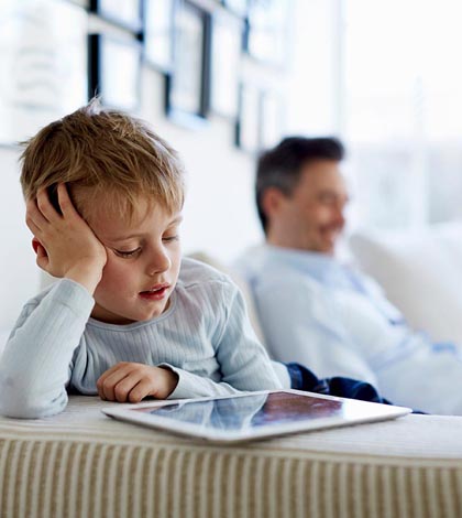 Father and son sitting on sofa using digital tablets